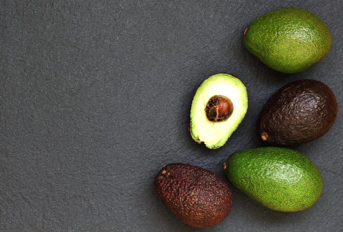 Different varieties of avocados on a dark background.