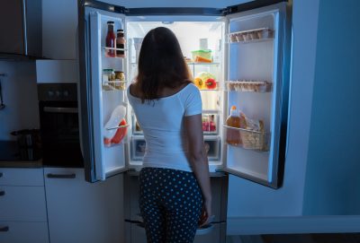 A woman looking into a open fridge at night.
