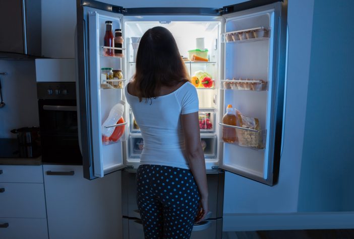 A woman looking into a open fridge at night.