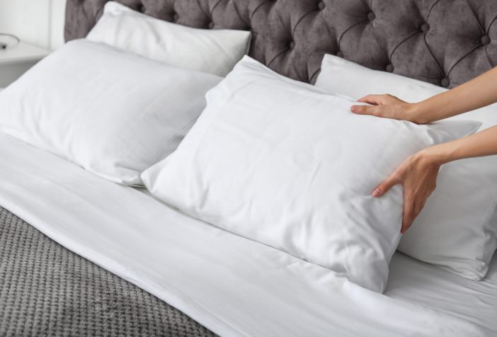 Someone placing a white pillow on a bed.