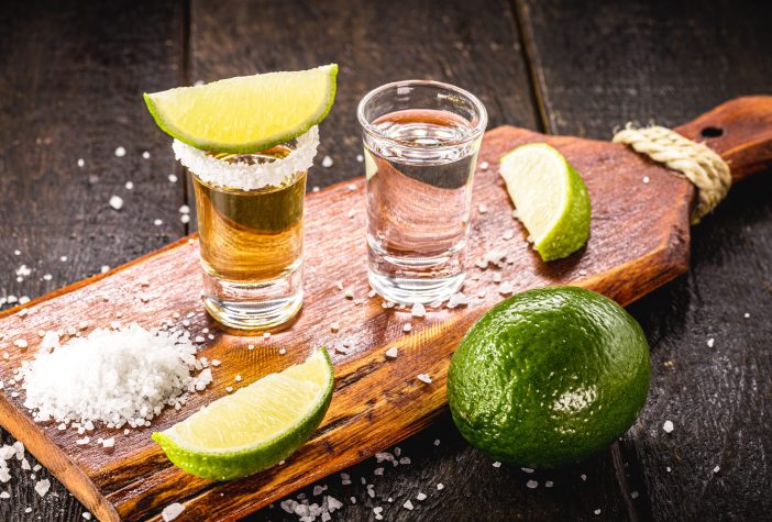 Shots of gold and silver tequila on a wooden board with salt and limes.