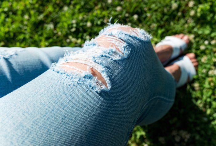 Person wearing distressed denim jeans.