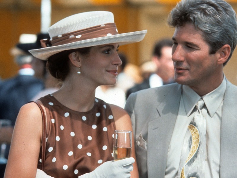 Screenshot from Pretty Woman, Julia Roberts on the left in a brown dress with polka dots and Richard Gere on the right in a grey suit