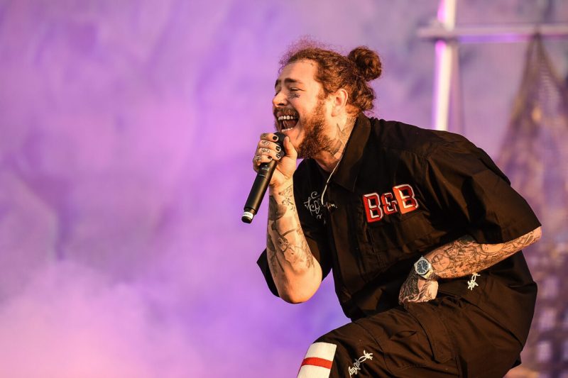 Post Malone sings into a microphoe in a purple, smokey background