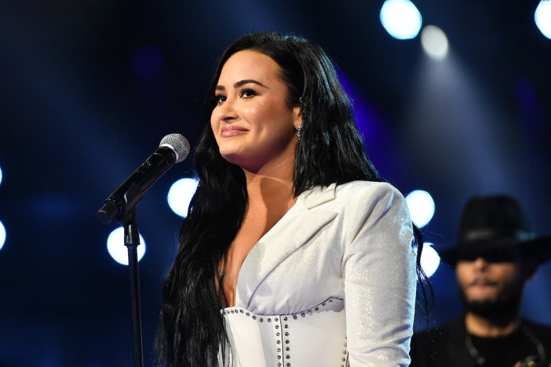 Demi Lovato smiles in a white dress standing at a mic at the 62nd Grammys