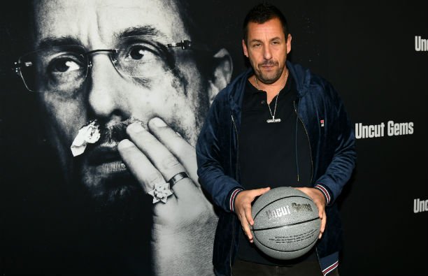 Adam Sandler wearing a black shirt with a blue jacket on the red carpet