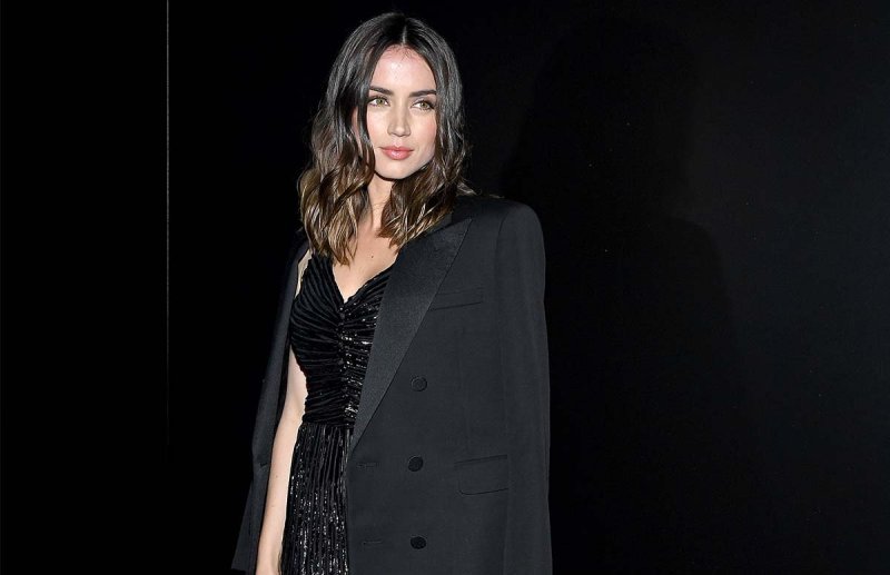 Ana de Armas in a black dress with a black coat over her shoulder.