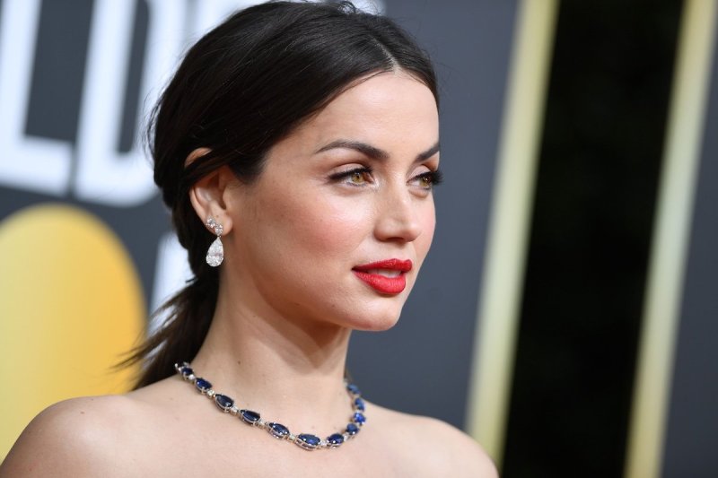 Ana de Armas smiles with red lipstick and her hair pulled back with a silver necklace on