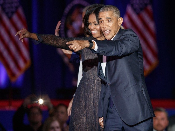 Barack and Michelle Obama hold hands and point offstage at the former President's farewell address