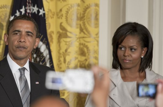Barack Obama, wearing a black suit, and Michelle Obama, in a tan suit, attend a White House event