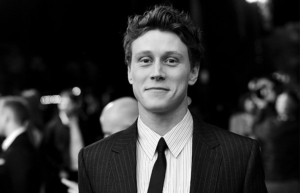 Black and white photo of George MacKay in a dark suit at a red carpet event