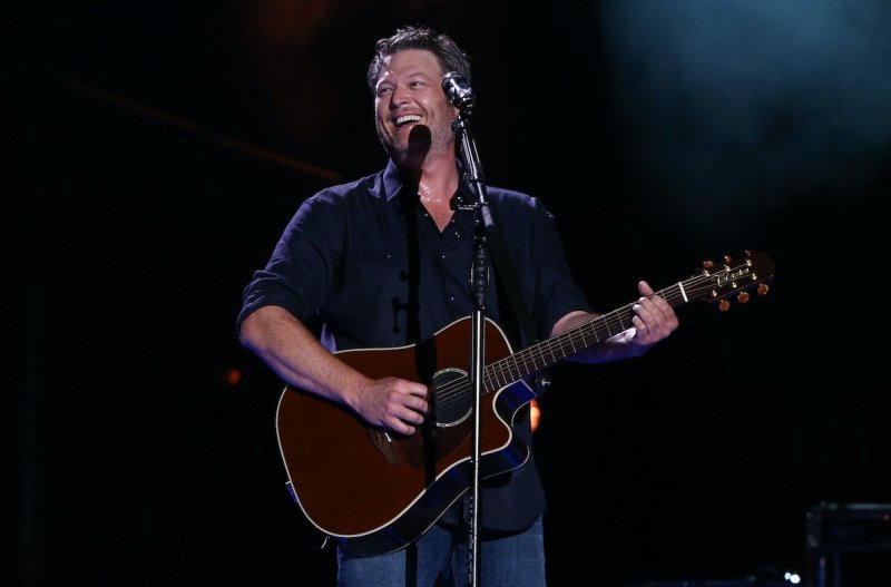 Blake Shelton singing in a navy shirt and jeans with a guitar on stage in 2017
