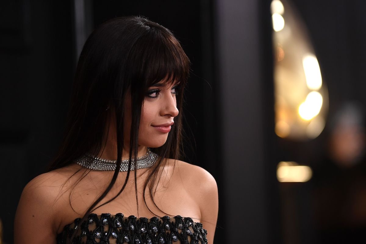 Camila Cabello in a black dress with her hair down looks and smiles to her left