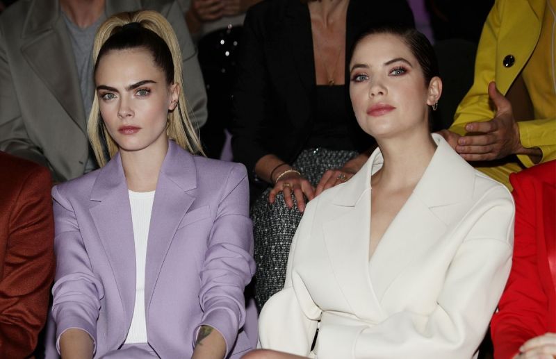Cara Delevingne wearing a purple suit sitting front row with Ashley Benson, who's wearing a white su
