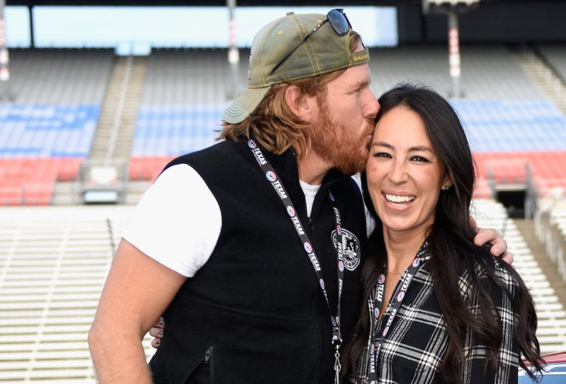 Chip Gaines in a black vest and white shirt kisses Joanna Gaines, in a plaid shirt, on the forehead