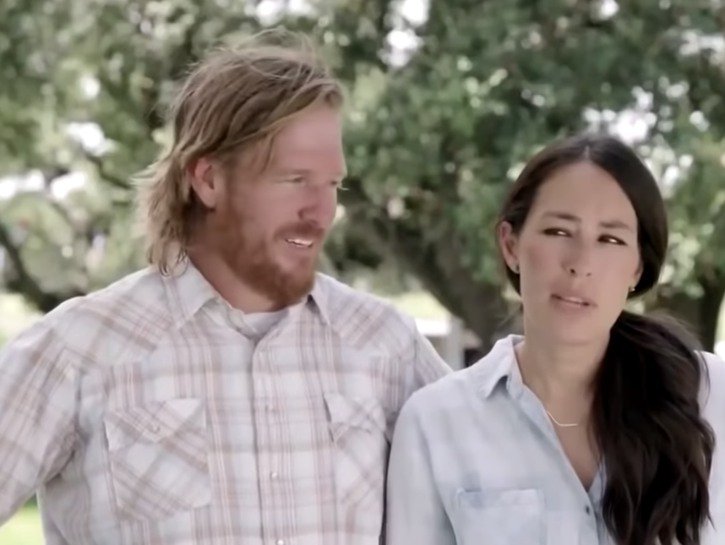 Chip Gaines wearing a checkered shirt standing with Joanna Gaines, in a blue top, on Fixer Uppers