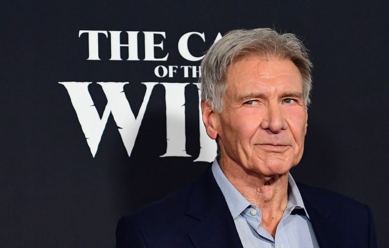 Close up shot of Harrison Ford looking to his right in a dark suit jacket and blue shirt on a black