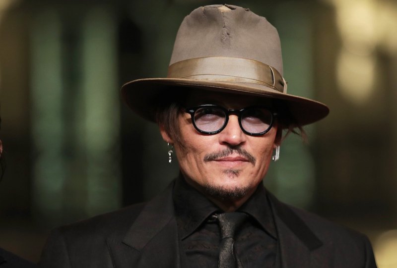 close up shot of Johnny Depp in a black on black suit, black rim glasses, and a tall tan fedora hat