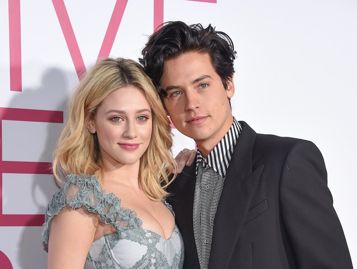Cole Sprouse smiles in a suit with Lili Reinhart in a dress