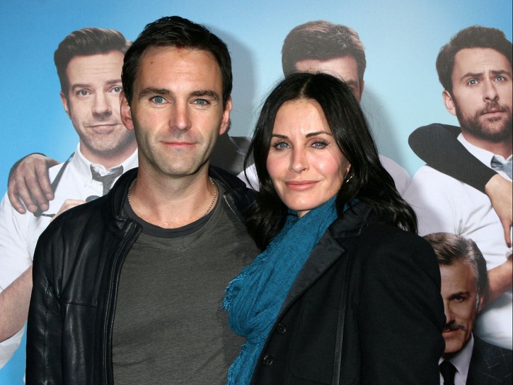 Courteney Cox smiles in a black jacket with boyfriend Johnny McDaid in a leather jacket