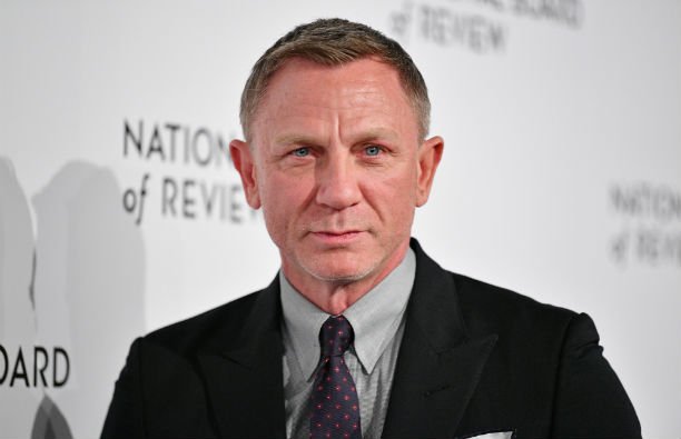 Daniel Craig wearing a dark suit with a light gray shirt on the red carpet.