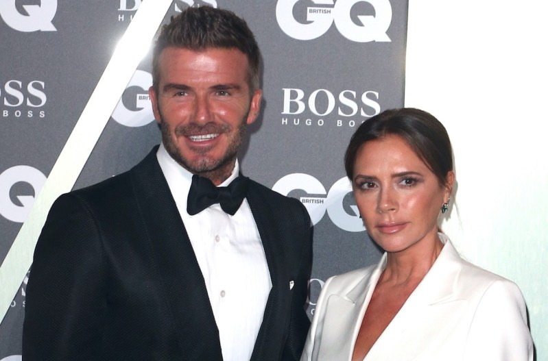 David Beckham smiling in a tuxedo with wife Victoria Beckham in a white blazer
