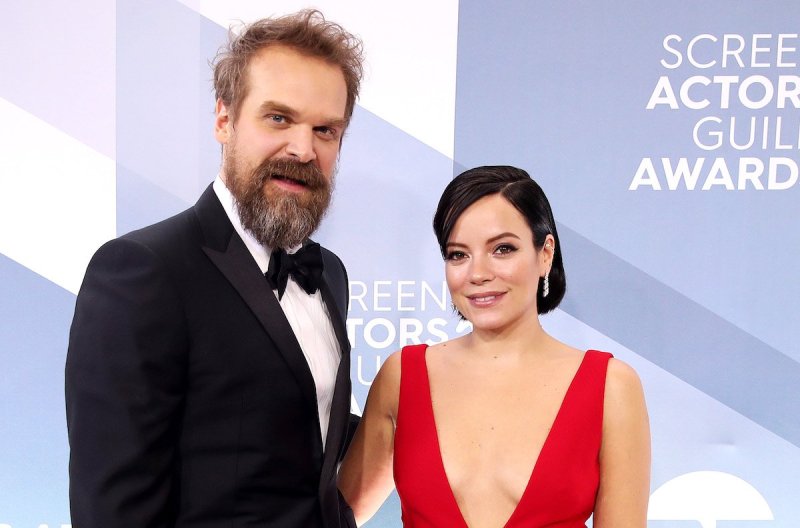 David Harbour in a tux and Lily Allen in a red dress with their arms around one another smiling
