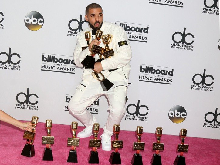 Drake wearing a white tux and holding several awards at the Billboard Music Awards