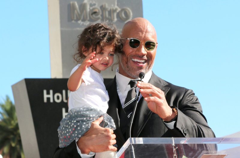 Dwayne The Rock Johnson standing at a podium holding his daughter Jasmine when she was younger.