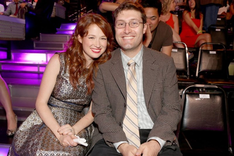 Ellie Kemper in a silver patterned dress smiles next to husband Michael Koman in a suit