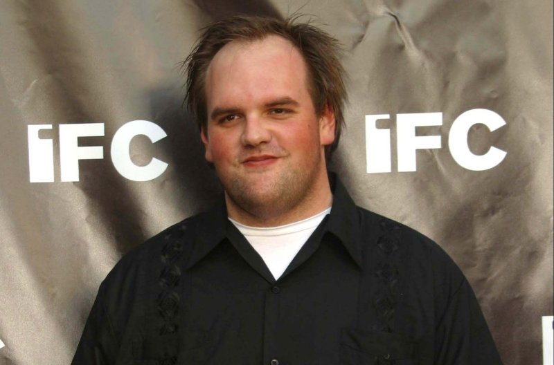 Ethan Suplee wearing a black shirt while standing against a dark gray background.