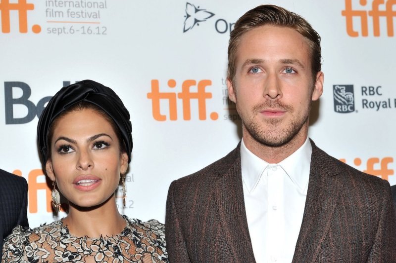 Eva Mendes in a silvery dress smiles next to Ryan Gosling in a brown suit jacket and white shirt