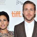 Eva Mendes in a silvery dress smiles next to Ryan Gosling in a brown suit jacket and white shirt