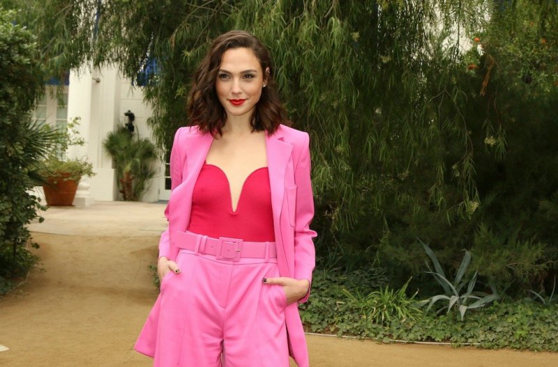 Gal Gadot smiles in a pink and red outfit standing outside