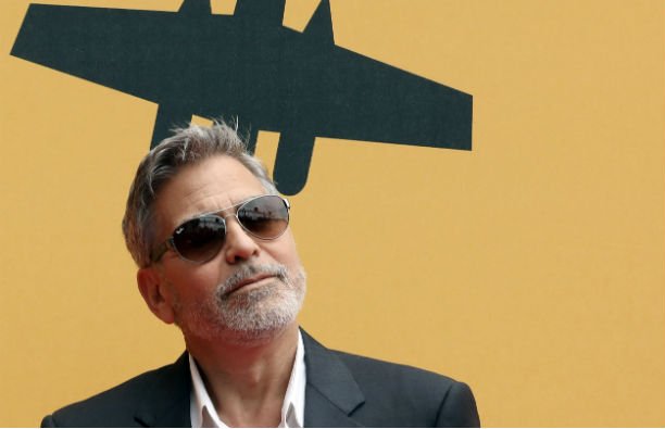 George Clooney wearing a black suit and sunglasses on the red carpet.