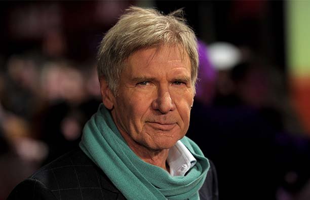 Harrison Ford in a green scarf, smirking at the camera