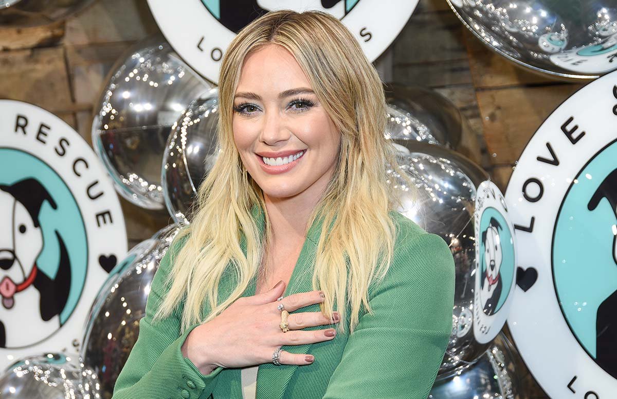 Hilary Duff smiling in a green jacket.