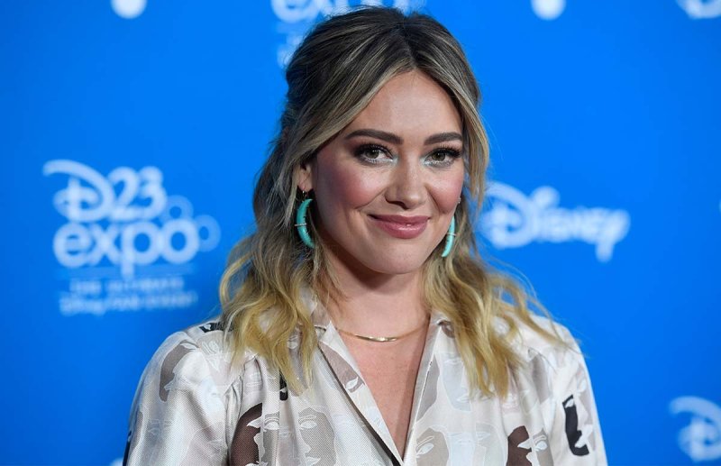 Hilary Duff smiling in front of a blue background