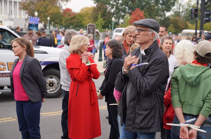 Jane Fonda, in red, and Ted Danson, in a dark jacket, stand with a crowd after their arrest