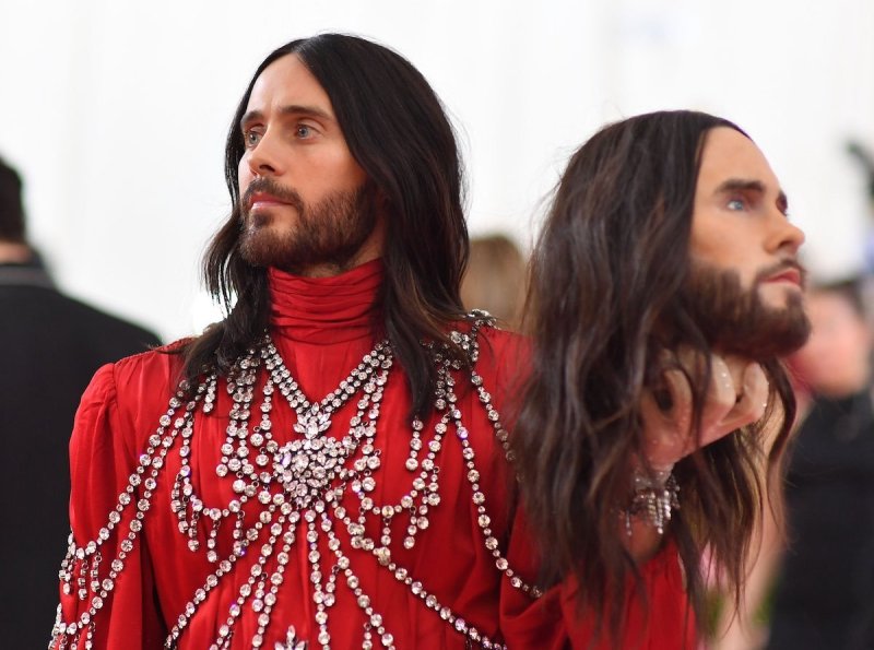 Jared Leto in a red gown holding a mannequin head that looks like him