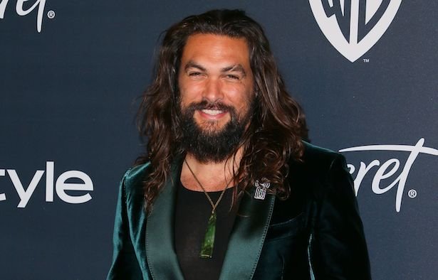 Jason Momoa with a raised eyebrow scar in a green tuxedo