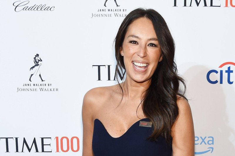 Joanna Gaines smiles at the camera in a blue dress against a white background