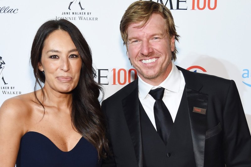 Joanna Gaines smiles in a blue dress next to Chip Gaines in a black suit and tie