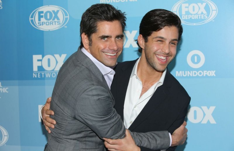 John Stamos wearing a gray suit embracing Josh Peck, who's wearing a black suit, on the red carpet