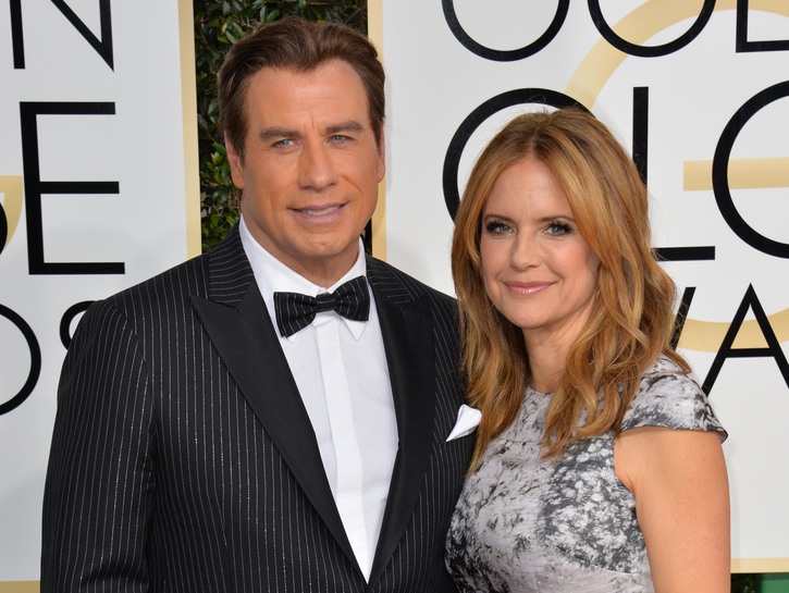 John Travolta wearing a black tux stands with Kelly Preston, in a gray dress, at the Golden Globes