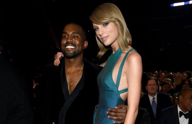 Kanye West wearing a black suit with no shirt standing with Taylor Swift, who's wearing a green dres