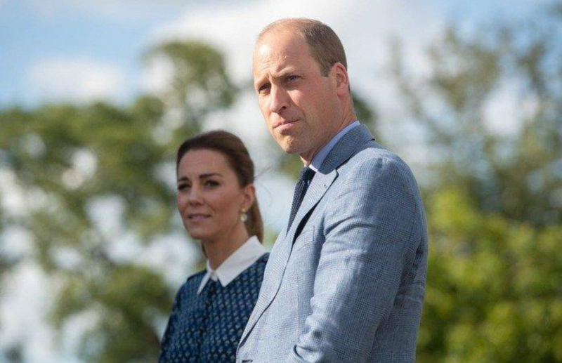 Kate Middleton wearing a blue dress standing with Prince William, who is wearing a gray suit.