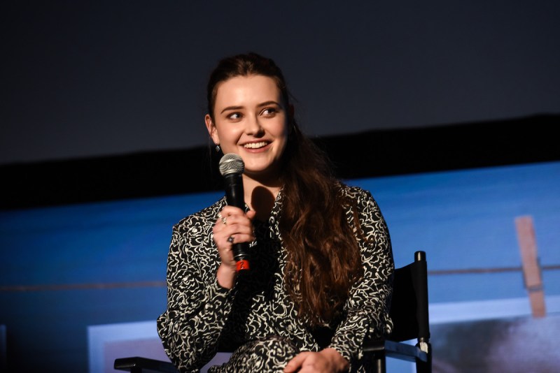 Katherine Langford sitting in a chair holding a mic dressed in a black and white patterned dress
