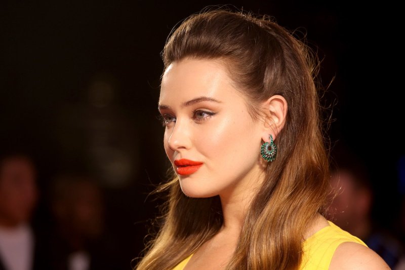 Katherine Langford smiles to the camera's left, wearing a yellow dress and bright red lipstick