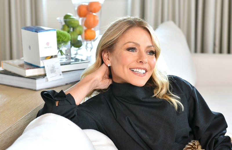 Kelly Ripa in a black shirt sitting back on a couch